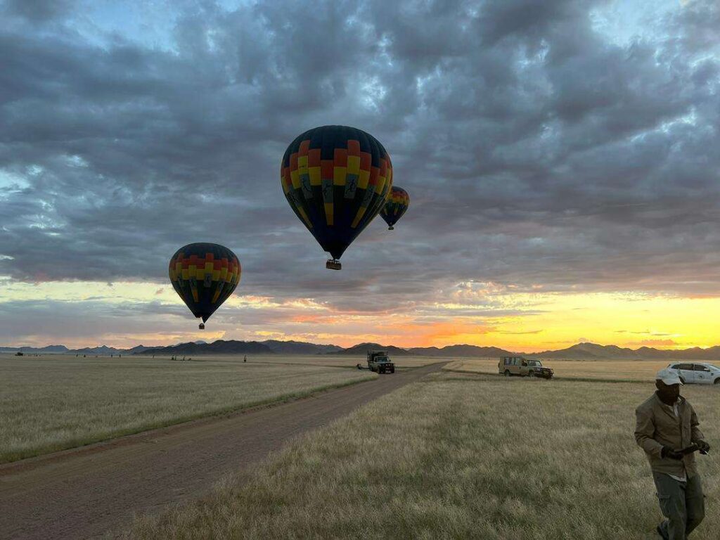 Three hot-air balloons lifting off the plains at sunrise over the Namib
